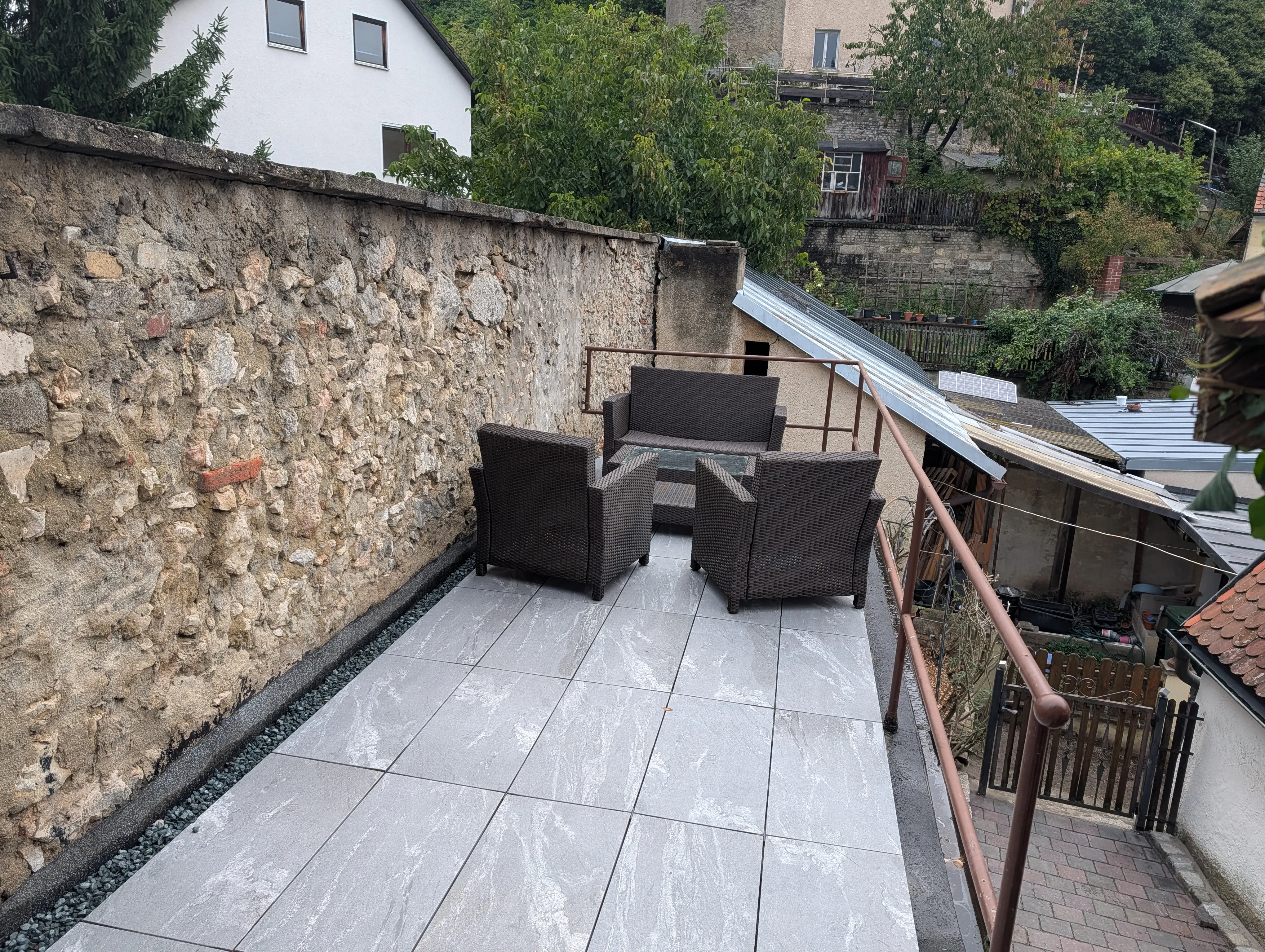 Die Terrasse mit Plattenbelag und Lounge-Möbeln aus Poly-Rattan, entlang der alten Bruchsteinmauer.