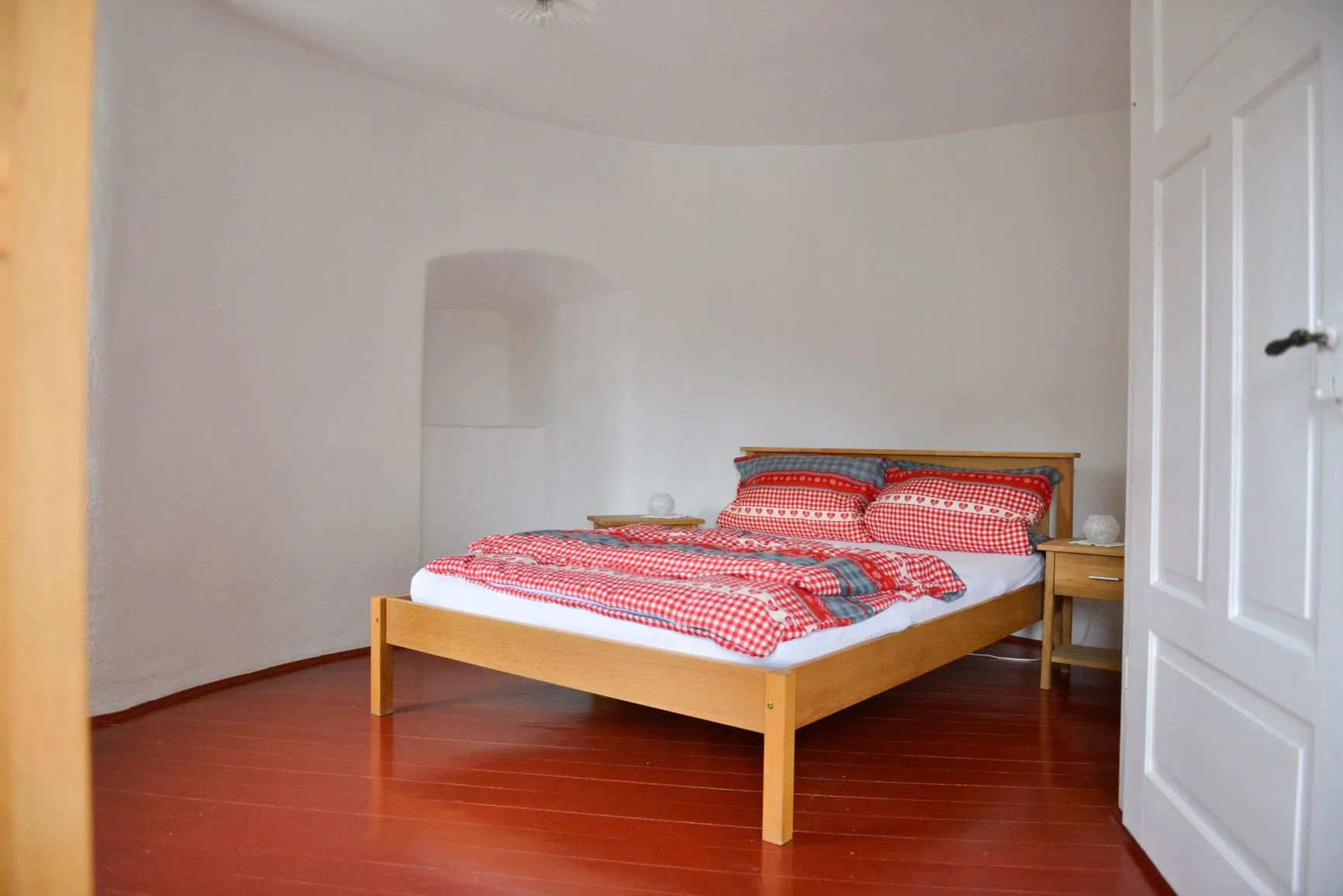 Das Schlafzimmer im Obergeschoss mit Doppelbett und rot-weiß karierter Bettwäsche.